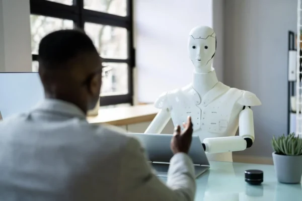 A man at a desk interacts with a robot located directly in front of him.