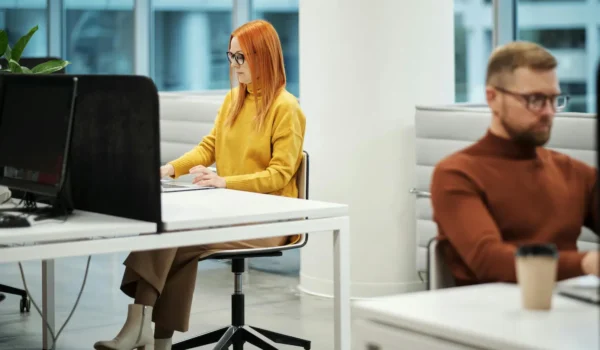 Two professionals working in a contemporary office environment with computers and casual attire.