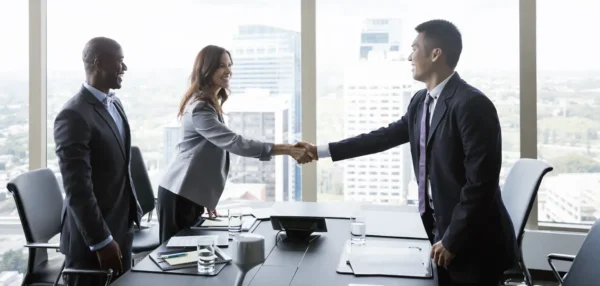Business professionals shaking hands in a modern office setting, symbolizing agreement and collaboration.